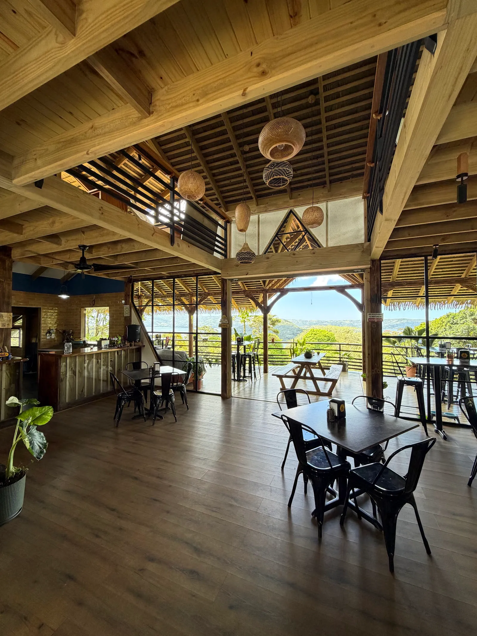 Inside the Bee Stop café: timber trusses, woven lanterns and tables open to a Lake Arenal view